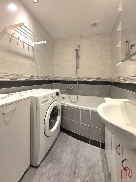 Bathroom with a bathtub, washing machine, and tiles in a 2-room apartment.