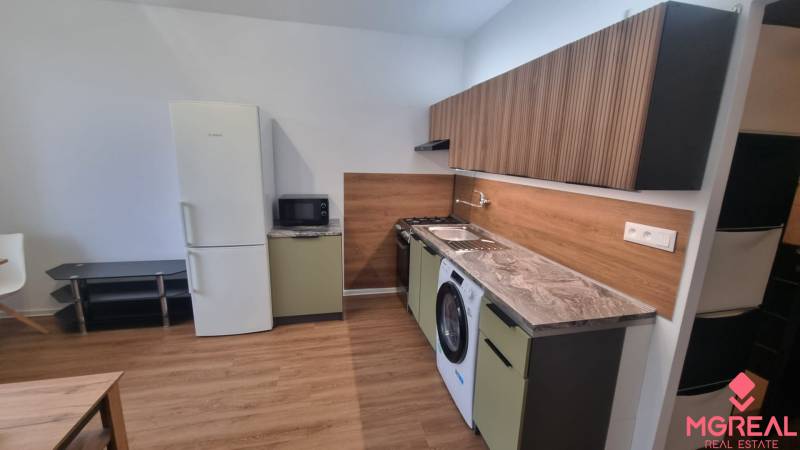 A kitchen unit in a studio apartment with a wood-patterned floor and appliances.