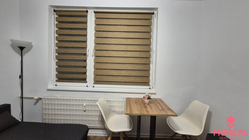 Dining area with a wooden table and two white chairs in a studio apartment.