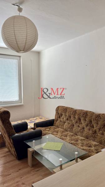 Studio apartment with a sofa, armchair, and a table, wooden decor flooring, paper lamp.