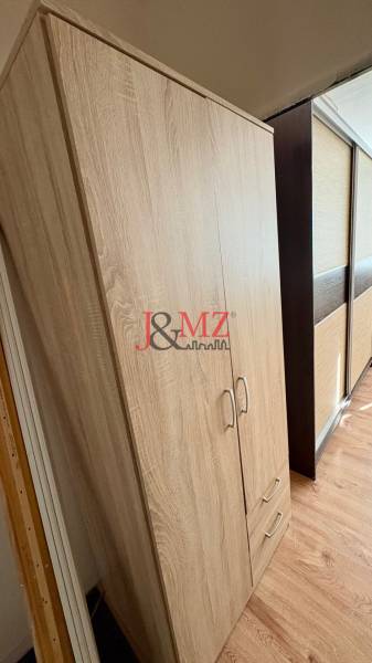 A wardrobe in a studio apartment with a wood-patterned floor and sliding doors.