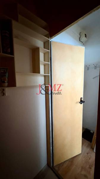 Open door, wall with shelves, hooks. Studio apartment with wood-patterned flooring.