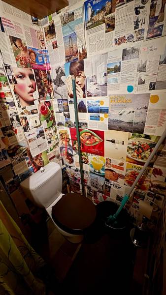 Bathroom with a toilet and walls covered with magazine clippings in a studio apartment.