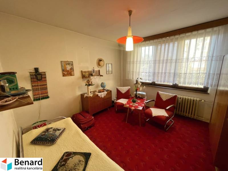 A room in a 3-room apartment with older furniture, a red carpet, and decorations.