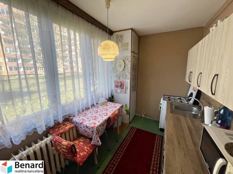 A kitchen in a 3-room apartment with a wooden decor floor and a large window with curtains.