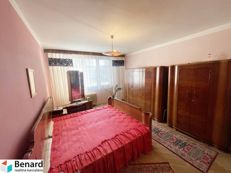 A bedroom in a 3-room apartment with red bedding and wooden wardrobes.