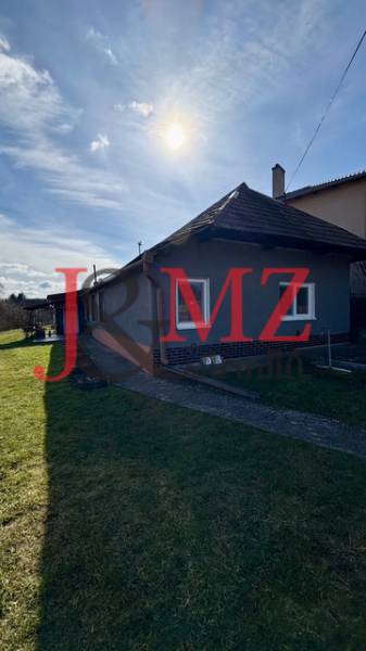 A family house in Mýtne Ludany, surrounded by a garden, with a blue sky and sunshine.