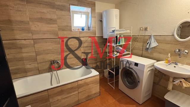 Bathroom in a family house with a bathtub, washing machine, and floor with wooden decor.