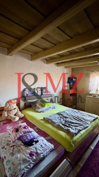 A bedroom in a family house with a wooden ceiling, a bed, and a plush teddy bear.