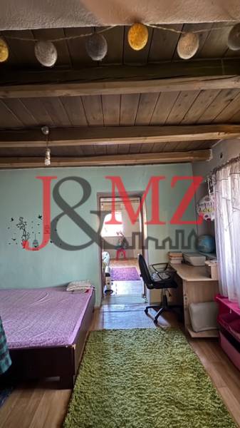 A room with a wooden floor decor, a bed, a work desk, and decorative beams on the ceiling.