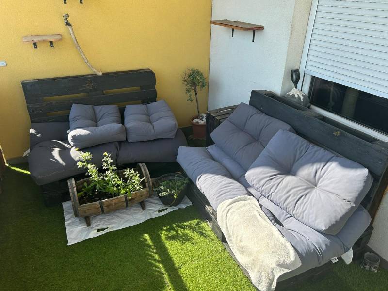 The 3-room apartment has a terrace with pallet furniture, cushions, and plants on artificial grass.