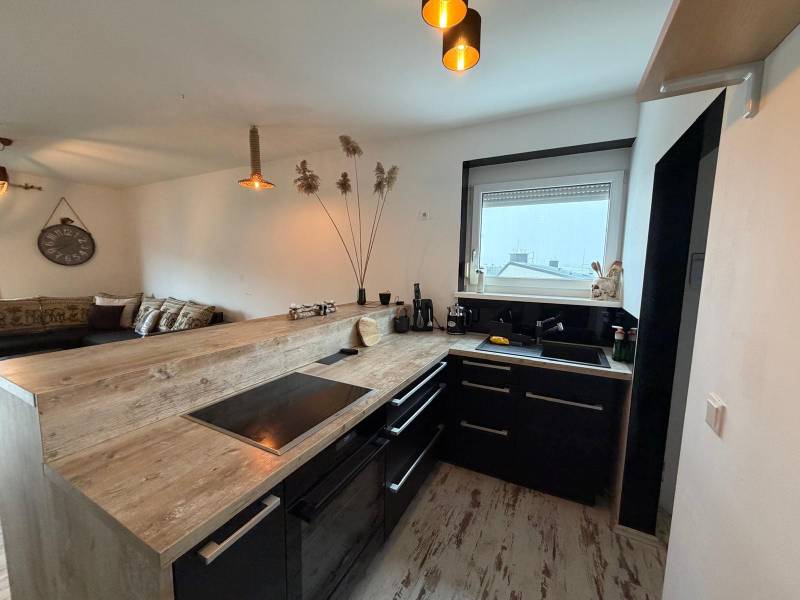 A kitchen with black furniture, a bar counter, and a wooden decor floor in a 3-room apartment.