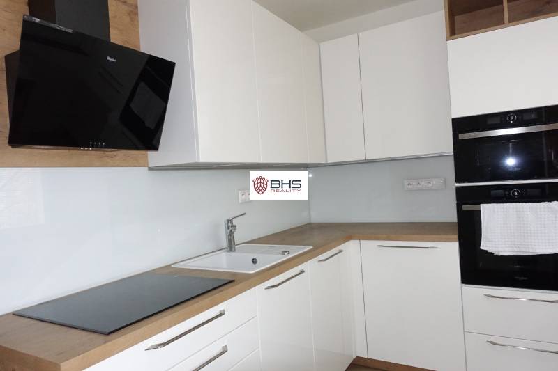 A kitchen with white cabinets and appliances, complemented by a wood-patterned floor in a three-room apartment.