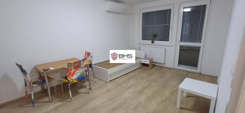 3-room apartment with wood-patterned flooring, a table, chairs, and a bed.