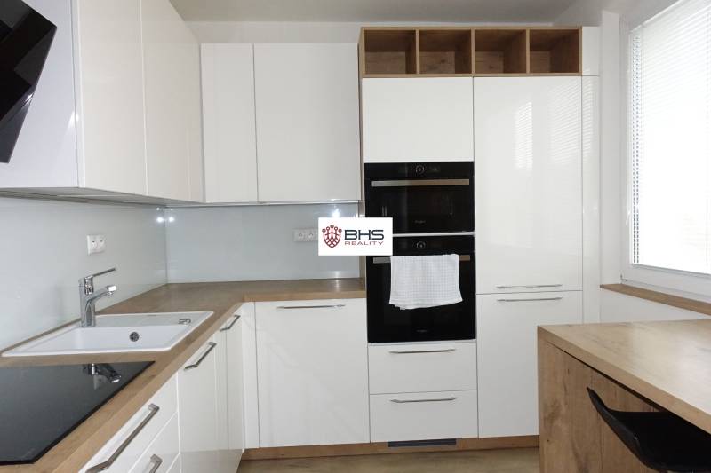 Modern kitchen with white cabinets and wood-patterned flooring in a three-room apartment.