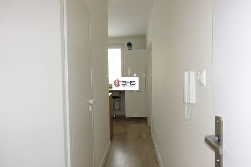 A narrow hallway with a wooden decor floor leads to the kitchen in a 3-room apartment.