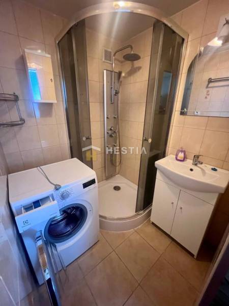 A bathroom with a washing machine, shower, sink, and mirror in a 3-room apartment.