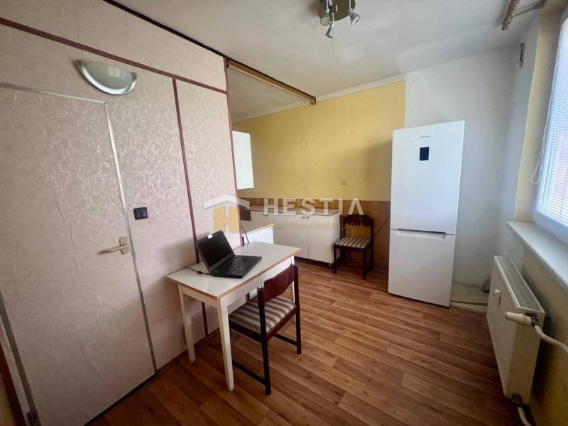 A kitchen in a 3-room apartment with a desk, refrigerator, and wooden floor.