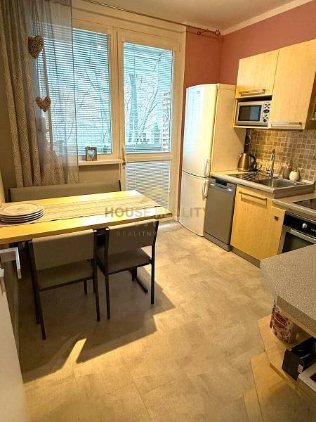 A kitchen in a 3-room apartment with a dining table, light cabinets, and a refrigerator.