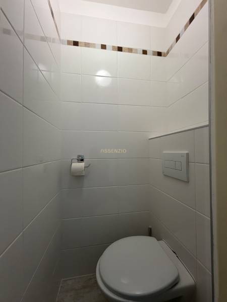 Bathroom in a studio apartment with white tiles and a wall with a decorative strip.