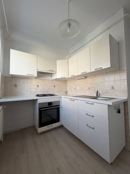 A kitchen in a studio apartment with white cabinets, a cooktop, and a wooden decor floor.