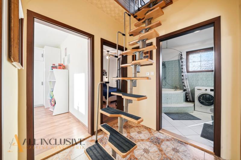 Spiral staircase, bathroom with a washing machine, and floor with wooden decor in a family house.