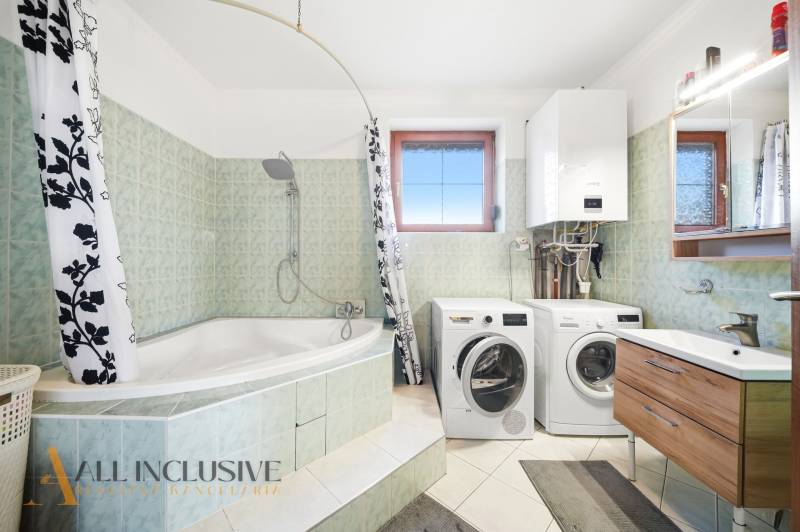 Bathroom with a bathtub, shower, washing machine, and dryer in a family house.