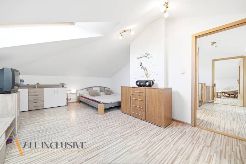 A bright bedroom with wood-patterned flooring, a dresser, and a bed in a family house.