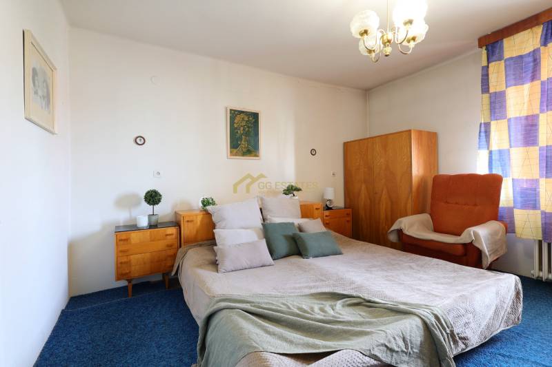 A bedroom with a large bed, wooden cabinets, and a chair in a family house.
