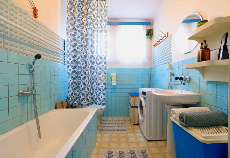 A bathroom in a family house with blue tiles, a bathtub, a washing machine, and a patterned curtain.