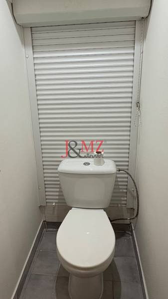 A toilet in a 2-room apartment with a white blind and tiles.