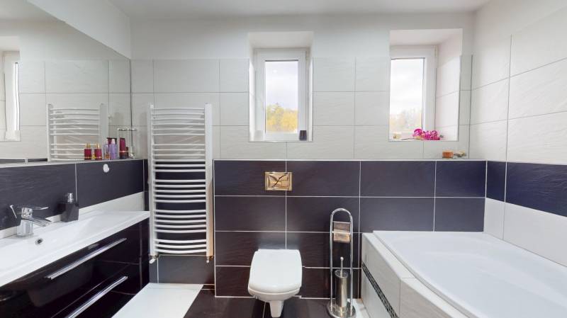 A bathroom in a family house with a bathtub, tiles, a sink, and windows on the wall.