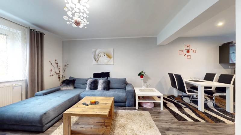Living room in a family house with a blue sofa, dining table, and floor with a wooden decor.