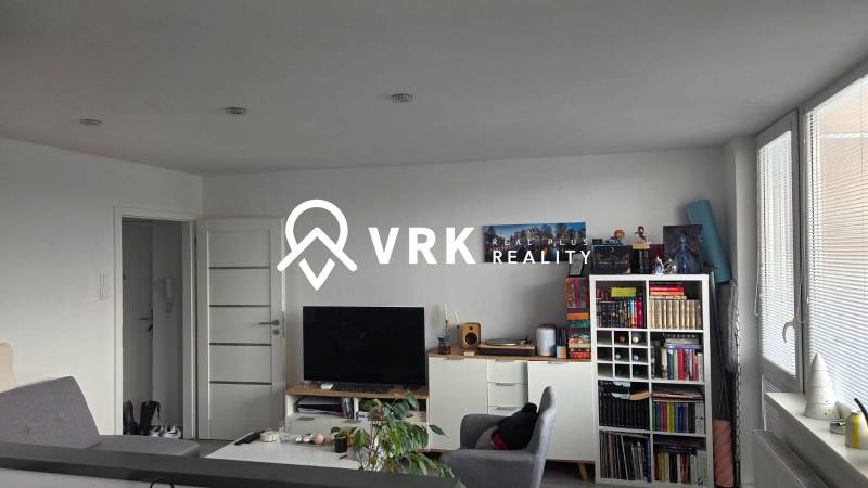 Living room of a three-room apartment with a bookshelf, television, and light-colored furniture.