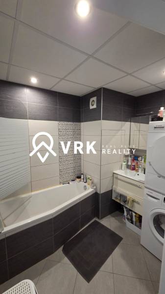 A bathroom in a 3-room apartment with a bathtub, washing machine, and dark tiles.