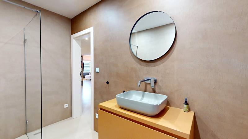 A bathroom in a family house with a sink, a round mirror, and a shower corner.