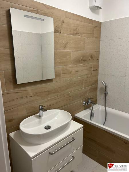 A bathroom in a 2-room apartment with a wooden decor floor and a bathtub.
