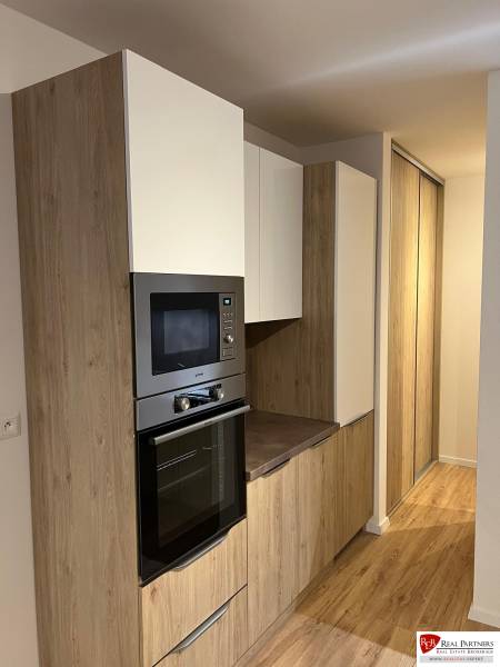 Kitchen area of a two-room apartment with a wooden decor floor and built-in cabinets.