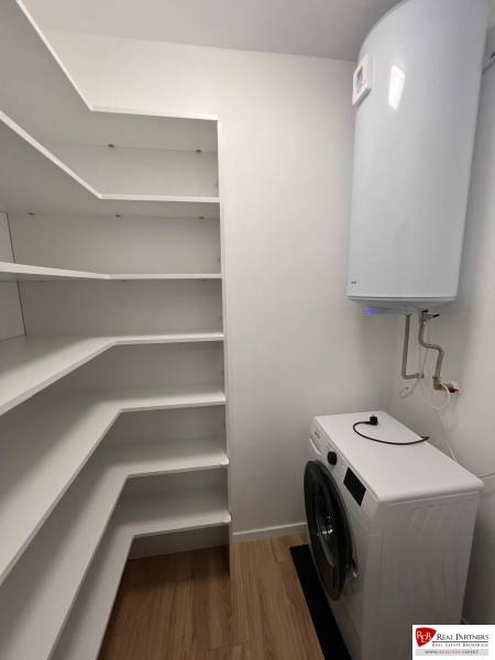 Laundry room in a 2-bedroom apartment with shelves and wood-patterned flooring.