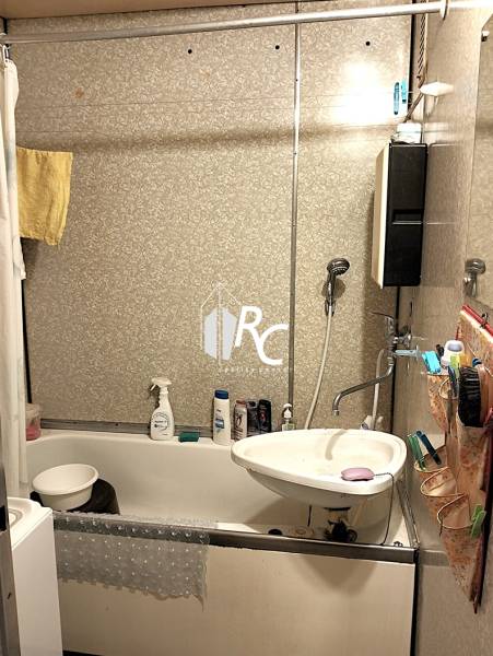 A bathroom in a 2-room apartment with a bathtub, sink, and tiled walls.
