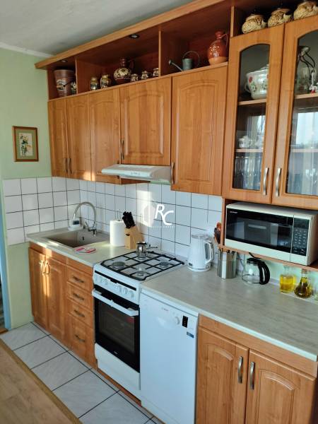 A kitchen in a 2-room apartment with wooden cabinets, a stove, and appliances.