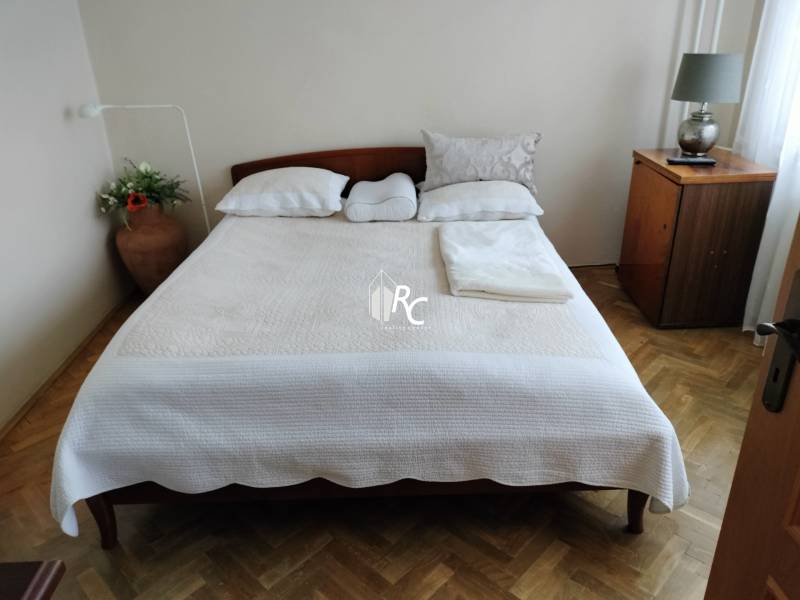 Bedroom with a double bed, wood-patterned flooring, and a nightstand in a two-room apartment.