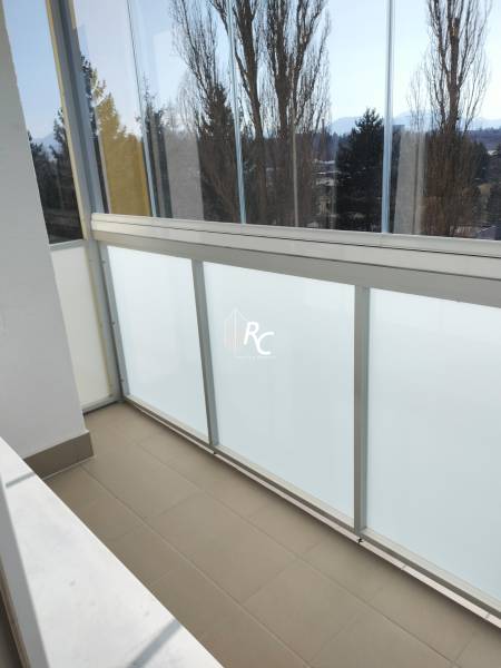 A glazed balcony in a 2-room apartment with a view of trees and mountains.