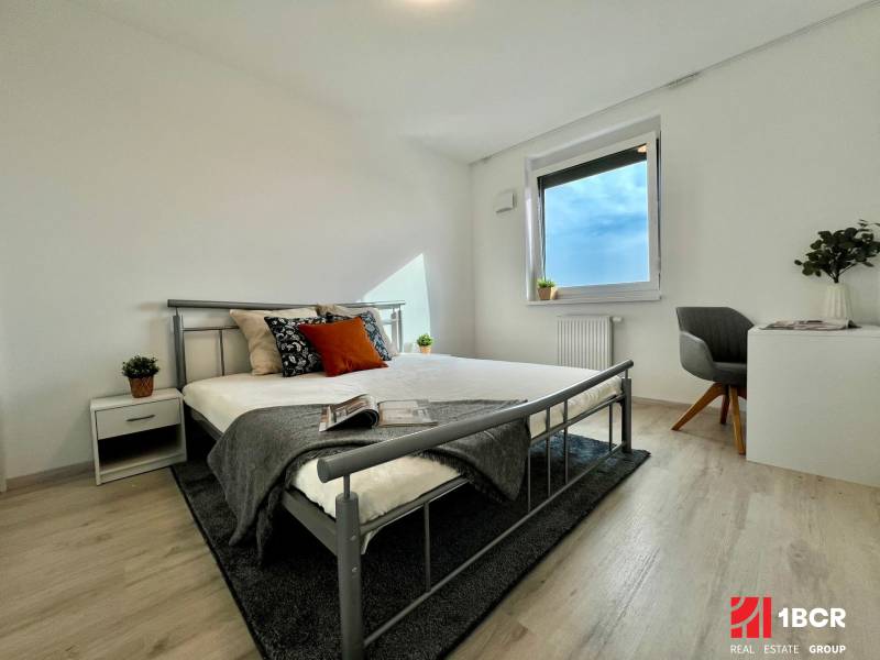 A bedroom in a two-room apartment with a wood-patterned floor and a metal bed.