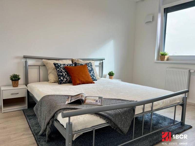 Bedroom in a 2-room apartment with a metal bed, wooden decor flooring, simple decorations.