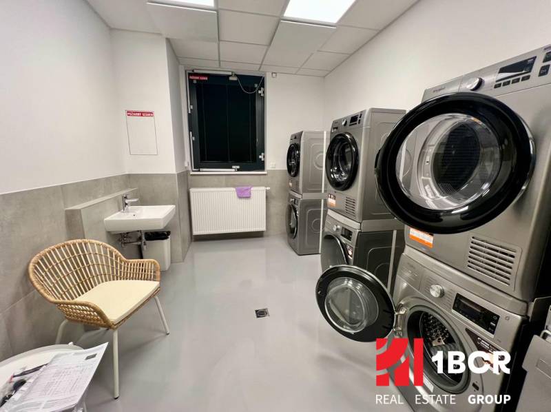 Laundry room with washing machines, dryers, a sink, and a chair in a 2-room apartment.