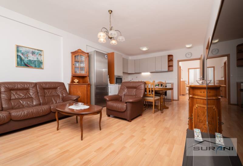 Living room with a leather sofa, dining table, and kitchen, 3-room apartment, floor with wooden decor.