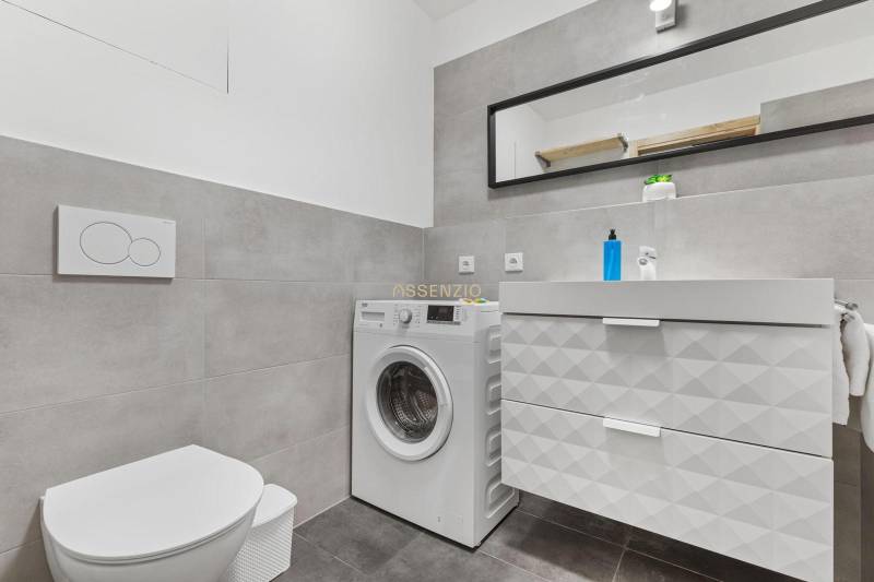 Bathroom with a washing machine and a sink, tiles, cabinet with drawers, mirror in a studio apartment.
