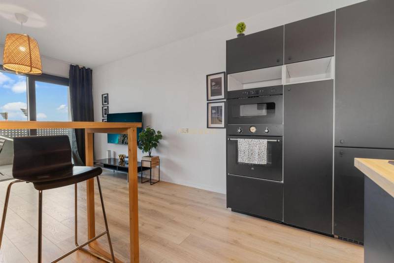 A kitchen in a studio apartment with black appliances and a wooden decor floor.
