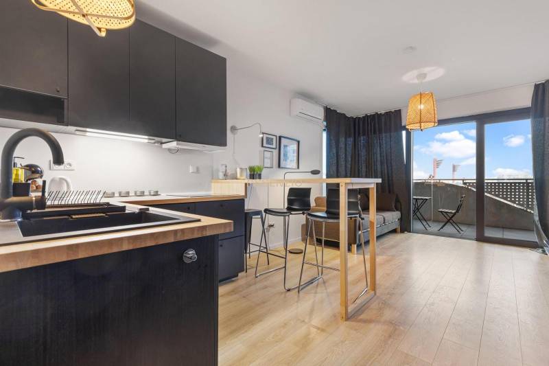 A kitchen with black cabinets, a bar counter, and a wood-patterned floor in a studio apartment.